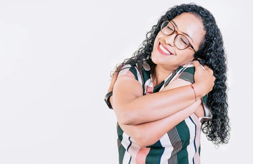 Smiling young woman hugging herself with self love. Self love concept. Afro woman hugging herself isolated