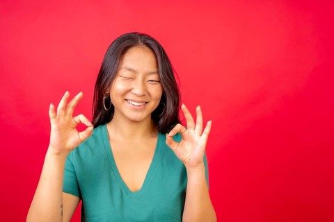 Studio photo with red background of a young chinese woman gesturing ok with hands and winking