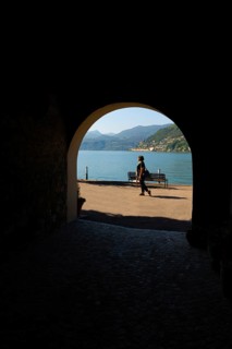 Woman Walking in an Old Beautiful Street Tunnel with Arch from Brusino Arsizio on the Waterfront in a Sunny Summer Day and with Lake Lugano and Mountain View over Morcote