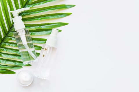 Two transparent cosmetic bottle with spray head moisturizer green leaf against whit e background