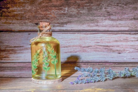 Glass bottle with lavender oil with lavender branches inside on a wooden table
