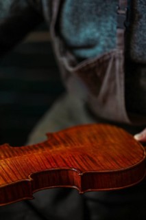Senior luthier violin maker holding a fresh varnished instrument in his hands in Cremona