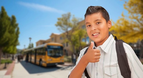 Excited young hispanic boy wearing a backpack giving two thumbs up on campus