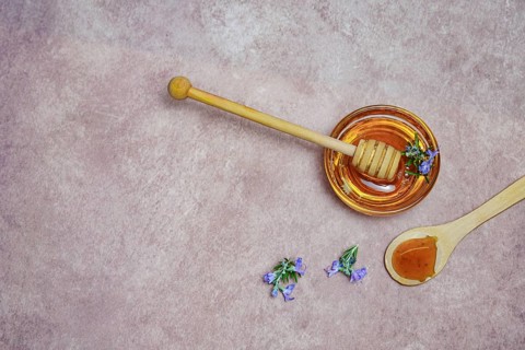 Top view of natural rosemary honey in a glass bowl with a wooden spoon and fresh rosemary branches in blossom