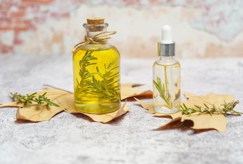 Bottle of rosemary essential oil with fresh branches inside and dropper with oil ready for use on dry leaves