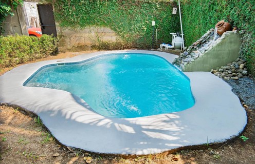 Crystal water home pool surrounded by a garden. Swimming pool designs for the home. Home swimming pool maintenance concept. Homemade swimming pool in a garden