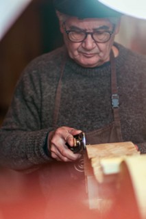 Senior expert luthier artisan violin maker carve sculpt chisel ribs of a new classical model cello in workshop Cremona Italy
