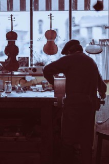 Senior expert luthier artisan violin maker carve sculpt chisel ribs of a new classical model cello in workshop Cremona Italy