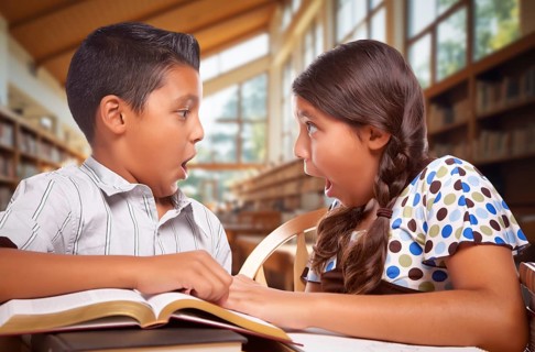 Two hispanic school kids in a library with a shocked expression on their faces