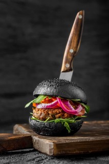 Front view veggie burger with black buns cutting board with knife