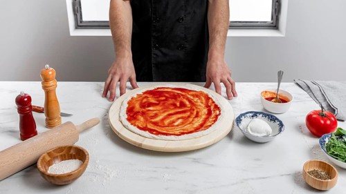 High angle man spreading tomato sauce pizza dough