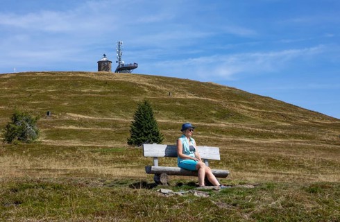 Hiker sitting on a bench on the Gerlitzen with view to the Kanzelhoehe