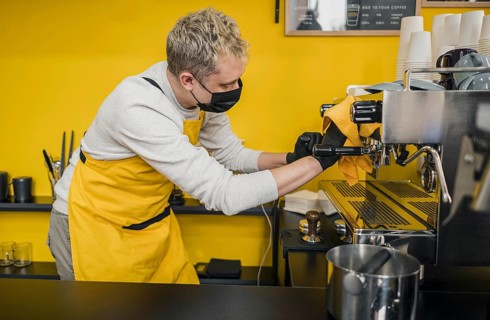 Side view male barista with medical mask cleaning coffee machine