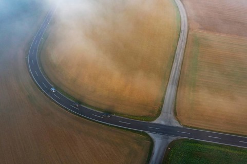 Drone view of a rural landscape shrouded in dense morning fog with a road junction near Prambachkirchen