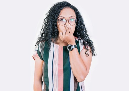 Displeased afro girl holding her nose isolated. Disgusted young afro woman covering nose. Woman in glasses covering nose from a bad smell isolated