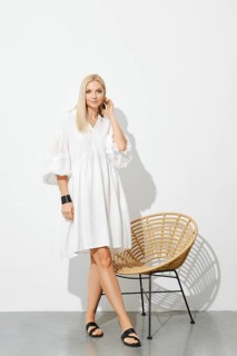 Beautiful woman in white sundress standing by wicker chair in sunny room