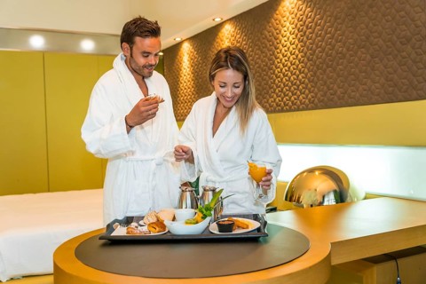 Happy newlywed couple wearing bathrobe eating breakfast in a luxury hotel room