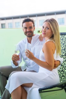 Vertical portrait of lovers celebrating love with champagne sitting on a chair in the terrace of an hotel