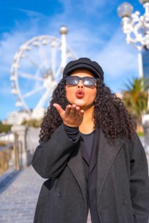 Vertical portrait of a latin stylish woman blowing a kiss standing in the city in a sunny day of winter
