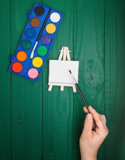 Elevated view hand holding paint brush mini easel watercolor palette