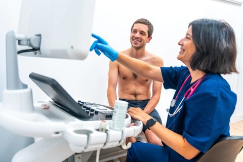 Cardiologist explaining the results on the screen of a echocardiogram to a patient sitting on stretcher in an hospital room