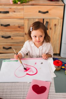 Little girl painting heart paper
