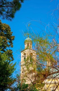Temple of the Holy Cross with Tower Against Blue Clear Sky and Tree Branch in a Sunny Day in Riva San Vitale