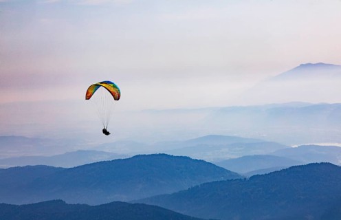 Paragliders high above the mountains with a view of the Klagenfurt basin and the Karawanken