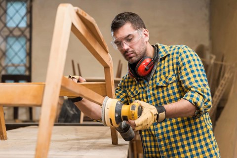Male carpenter wearing safety glasses using sander furniture workshop
