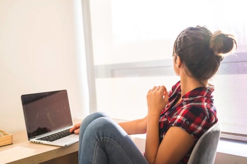 Woman looking at the window and dreaming while using laptop at home
