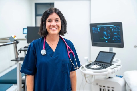 Happy cardiologist standing with arms crossed on a hospital next to modern equipment