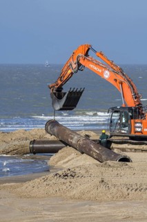 Hydraulic excavator installing pipeline during sand replenishment