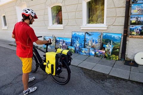 Cyclist looking at kitsch postcards and paintings in front of Hohenschwangau Castle