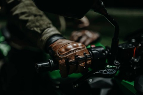 A motorcyclist in brown leather gloves sits on a motorcycle