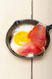 Fried egg sunny side up with Italian tyrolean speck smoked ham on a skillet
