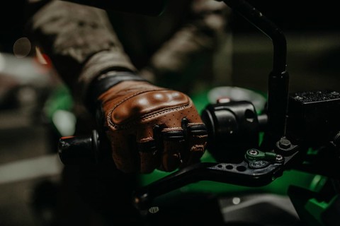 A motorcyclist in brown leather gloves sits on a motorcycle