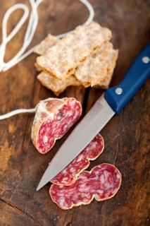 Slicing italian salame pressato pressed over old wood table