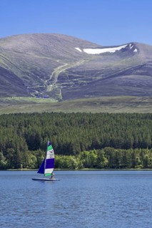 Sailing boat on Loch Morlich in front of the Cairngorm Mountains