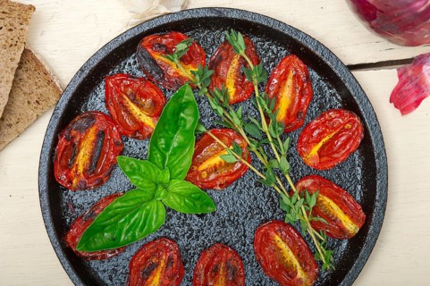 Oven baked cherry tomatoes with basil and thyme on a cast iron skillet