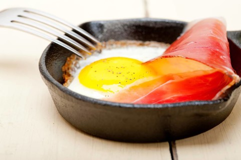 Fried egg sunny side up with Italian tyrolean speck smoked ham on a skillet