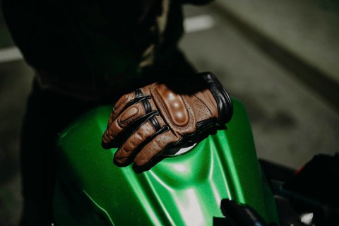 A brown leather motorcyclist glove lies on the tank of a green motorcycle