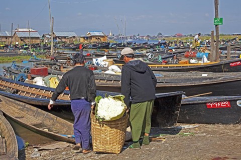 Open boats at lakeside village with traditional wooden houses on stilts in Inle Lake