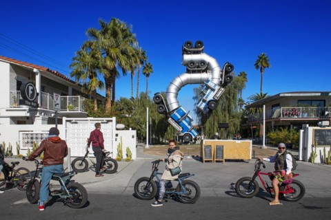 Group of cyclists on a guided tour in front of an artwork made of two art trailers