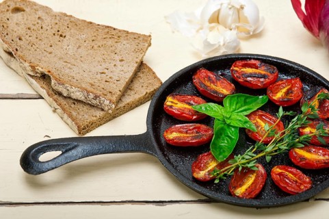 Oven baked cherry tomatoes with basil and thyme on a cast iron skillet