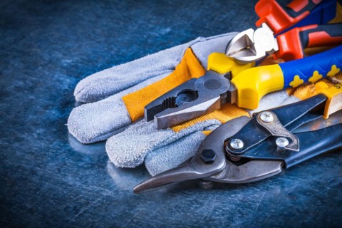 Safety gloves with pliers pliers and tin snips on scratched vintage metallic background construction concept
