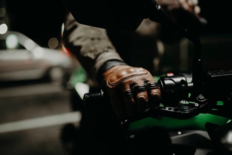A motorcyclist in brown leather gloves sits on a motorcycle