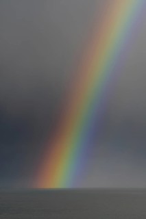 Colourful rainbow over sea water and approaching snow shower along the North Sea coast in winter