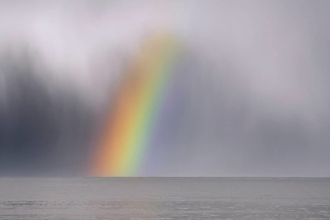 Colourful rainbow over sea water and approaching snow shower along the North Sea coast in winter