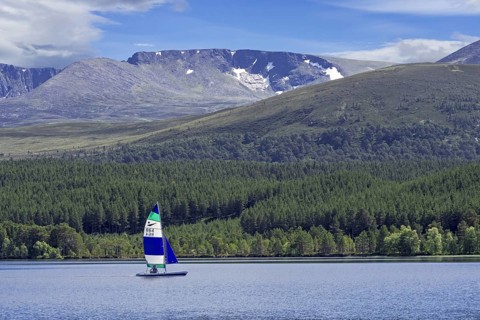 Sailing boat on Loch Morlich in front of the Cairngorm Mountains