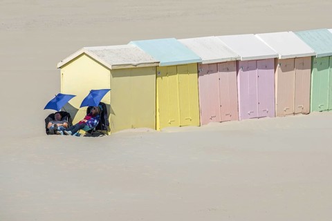 Two day trippers falling asleep under sunshades next to pastel coloured beach cabins at Berck